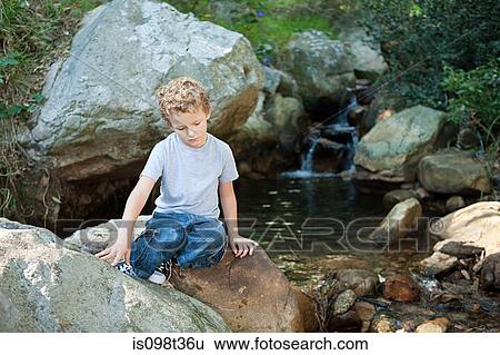 Boy sitting on rock by a river View Large Photo Image Stock Photograph - Boy sitting on rock by a river. Fotosearch