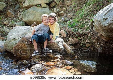 Boys sitting on rock by river View Large Photo Image Picture - Boys sitting on rock by river. Fotosearch