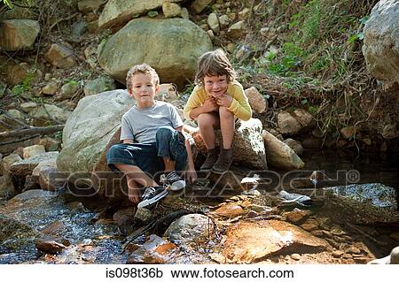 Boys sitting on rock by river View Large Photo Image Stock Image - Boys sitting on rock by river. Fotosearch