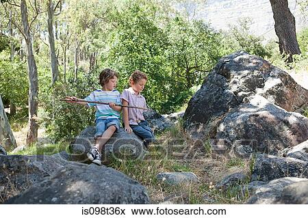 Boys sitting on rocks with stick View Large Photo Image Stock Photo - Boys sitting on rocks with stick. Fotosearch