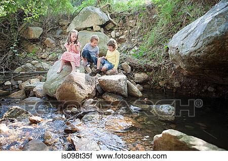 Stock Image - Children on rocks by river. Fotosearch