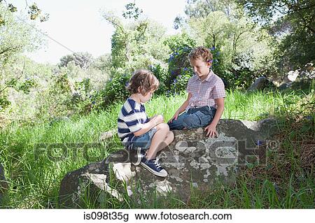 Two boys sitting on a rock View Large Photo Image Stock Image - Two boys sitting on a rock. Fotosearch