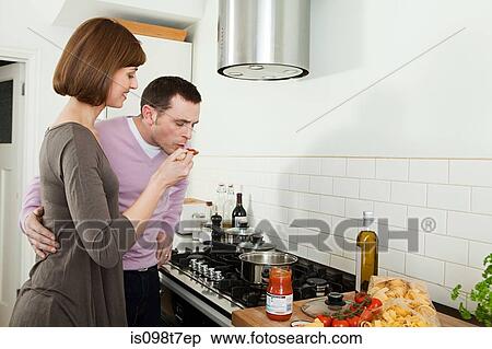 Stock Photography - Man tasting pasta sauce that wife is making. Fotosearch
