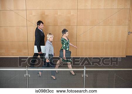Stock Image - Businesspeople walking through corridor. Fotosearch
