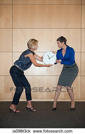 Stock Image - Businesswomen fighting over clock. Fotosearch