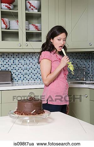 Young woman eating celery, watching chocolate cake View Large Photo Image Stock Image - Young woman eating celery, watching chocolate cake. Fotosearch