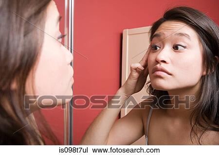 Stock Image - Young woman looking at reflection in mirror. Fotosearch