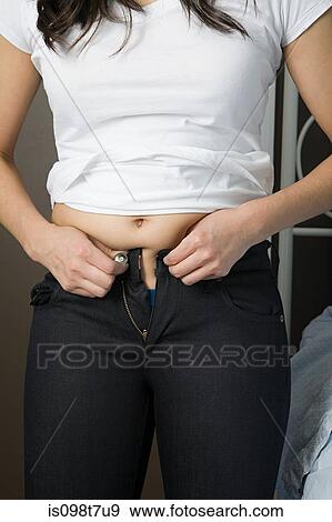 Stock Photo - Young woman trying to do up her jeans. Fotosearch