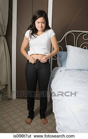 Young woman trying to do up her jeans View Large Photo Image Stock Photograph - Young woman trying to do up her jeans. Fotosearch