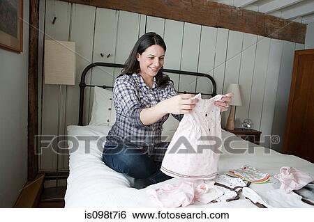 Stock Photograph - Expectant mother looking at baby clothes. Fotosearch