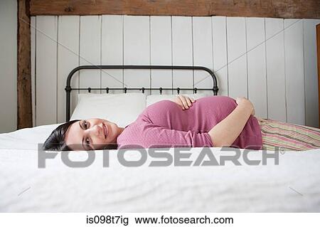 Stock Image - Pregnant woman lying on bed. Fotosearch