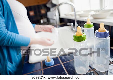 Stock Image - Pregnant woman washing baby bottles. Fotosearch
