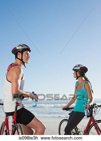 Stock Image - Young couple cycling at beach. Fotosearch