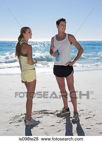 Stock Photo - Young couple with bottles of water on beach. Fotosearch