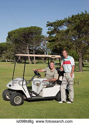 Stock Image - Two mature men in golf cart on golf course. Fotosearch