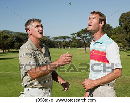 Stock Image - Two mature men playing golf together, tossing a coin. Fotosearch