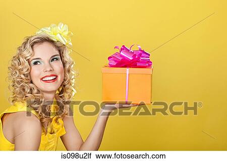 Young blonde woman holding birthday present against yellow background View Large Photo Image Stock Image - Young blonde woman holding birthday present against yellow background. Fotosearch