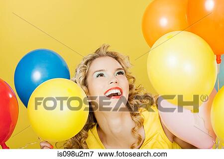Stock Photo - Young blonde woman with balloons against yellow background. Fotosearch