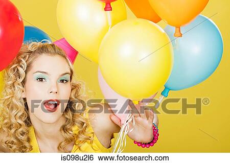 Stock Photograph - Young blonde woman with balloons against yellow background. Fotosearch