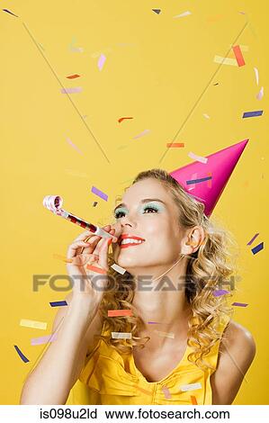 Stock Image - Young woman wearing party hat with party blower and confetti. Fotosearch