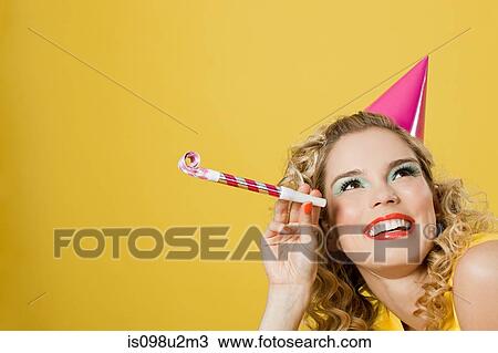Stock Image - Young woman wearing party hat with party blower. Fotosearch