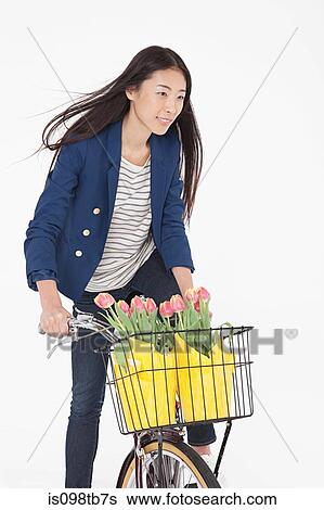 Stock Photograph - Woman riding bicycle with flowers in basket. Fotosearch