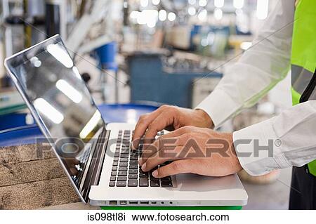 Stock Image - Mature man using laptop in factory. Fotosearch