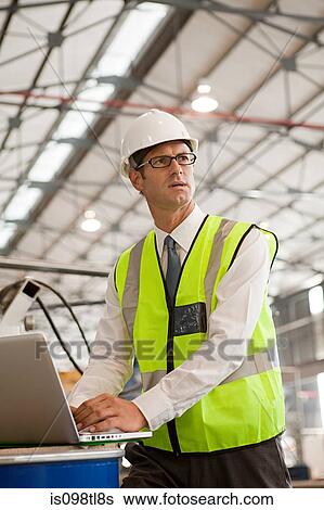Stock Photograph - Mature man using laptop in factory. Fotosearch