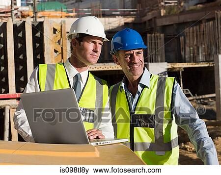 Mature men uusing laptop on construction site View Large Photo Image Stock Photo - Mature men uusing laptop on construction site. Fotosearch