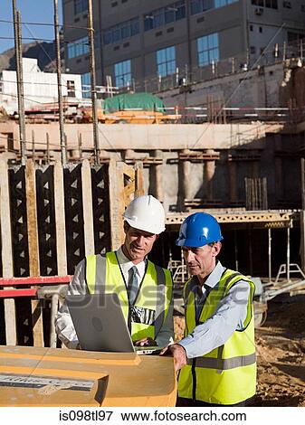 Mature men uusing laptop on construction site View Large Photo Image Stock Photo - Mature men uusing laptop on construction site. Fotosearch