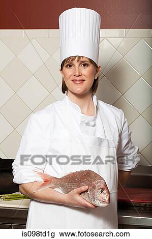Stock Image - Female chef holding raw fish in commercial kitchen. Fotosearch