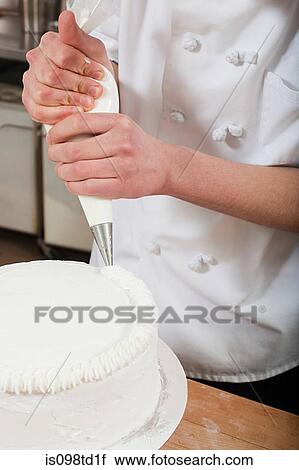 Stock Image - Female chef icing a cake. Fotosearch