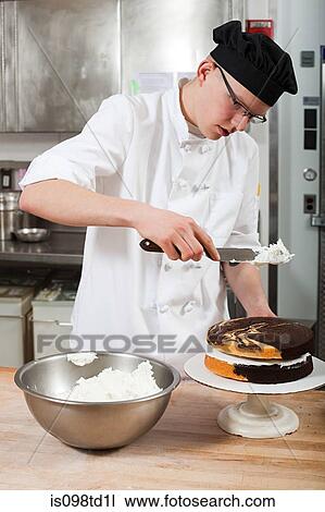 Stock Image - Male chef icing a cake in commercial kitchen. Fotosearch