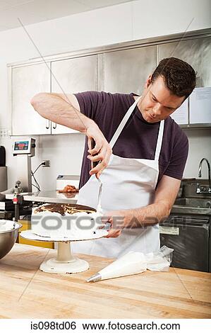 Stock Photograph - Male chef icing a cake in commercial kitchen. Fotosearch