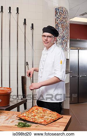 Stock Image - Male chef making pizza in commercial kitchen. Fotosearch
