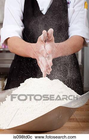 Stock Image - Male chef rubbing flour on hands in commercial kitchen. Fotosearch