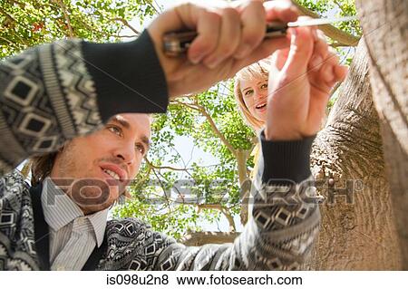 Stock Photo - Couple carving names on tree. Fotosearch
