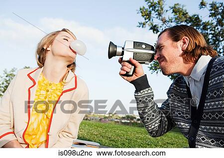 Stock Image - Man filming girlfriend blowing bubble gum. Fotosearch