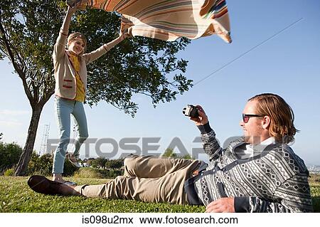 Young man photographing girlfriend as she shakes out a blanket View Large Photo Image Stock Photo - Young man photographing girlfriend as she shakes out a blanket. Fotosearch