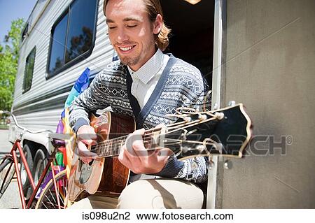 Young man playing guitar by caravan View Large Photo Image Stock Image - Young man playing guitar by caravan. Fotosearch