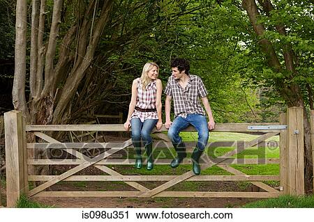 Stock Image - Young couple sitting on gate. Fotosearch