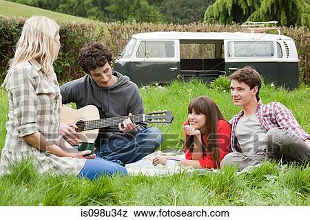 Young man playing guitar for friends in field View Large Photo Image Stock Photo - Young man playing guitar for friends in field. Fotosearch