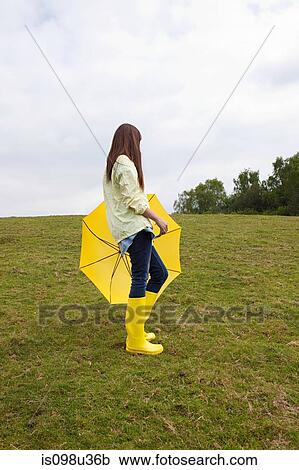 Stock Image - Young woman in field with umbrella. Fotosearch