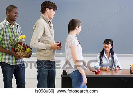 Stock Image - High school student giving teacher an apple. Fotosearch
