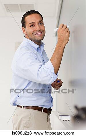 Stock Image - High school teacher using white board in classroom. Fotosearch