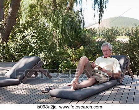 Stock Image - Senior man reading on sun lounger. Fotosearch