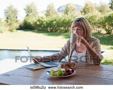 Stock Photo - Woman outdoors, reading newspaper and drinking coffee. Fotosearch