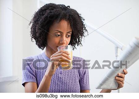 Stock Image - Woman with glass of juice and newspaper. Fotosearch