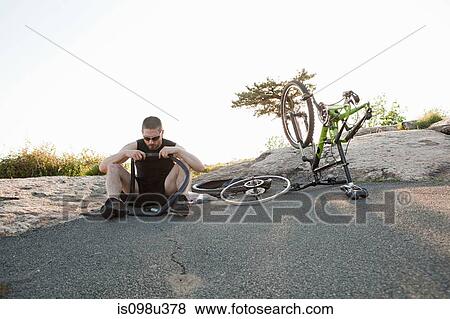 Male cyclist fixing punctured tyre View Large Photo Image Stock Photo - Male cyclist fixing punctured tyre. Fotosearch