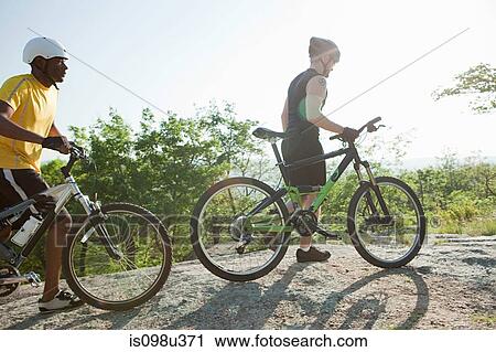 Two cyclists pushing bikes View Large Photo Image Stock Image - Two cyclists pushing bikes. Fotosearch